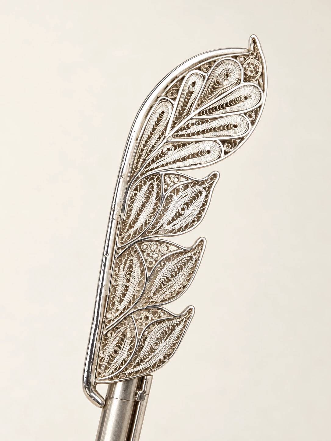 Filigree feather ornament mounted on a pen that is partly outside the frame