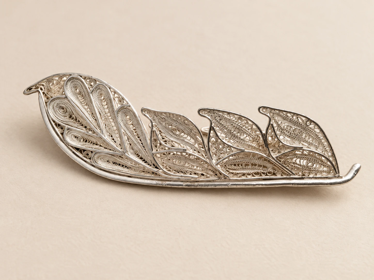 Oblique view of the feather ornament with filigree spirals and a central rib